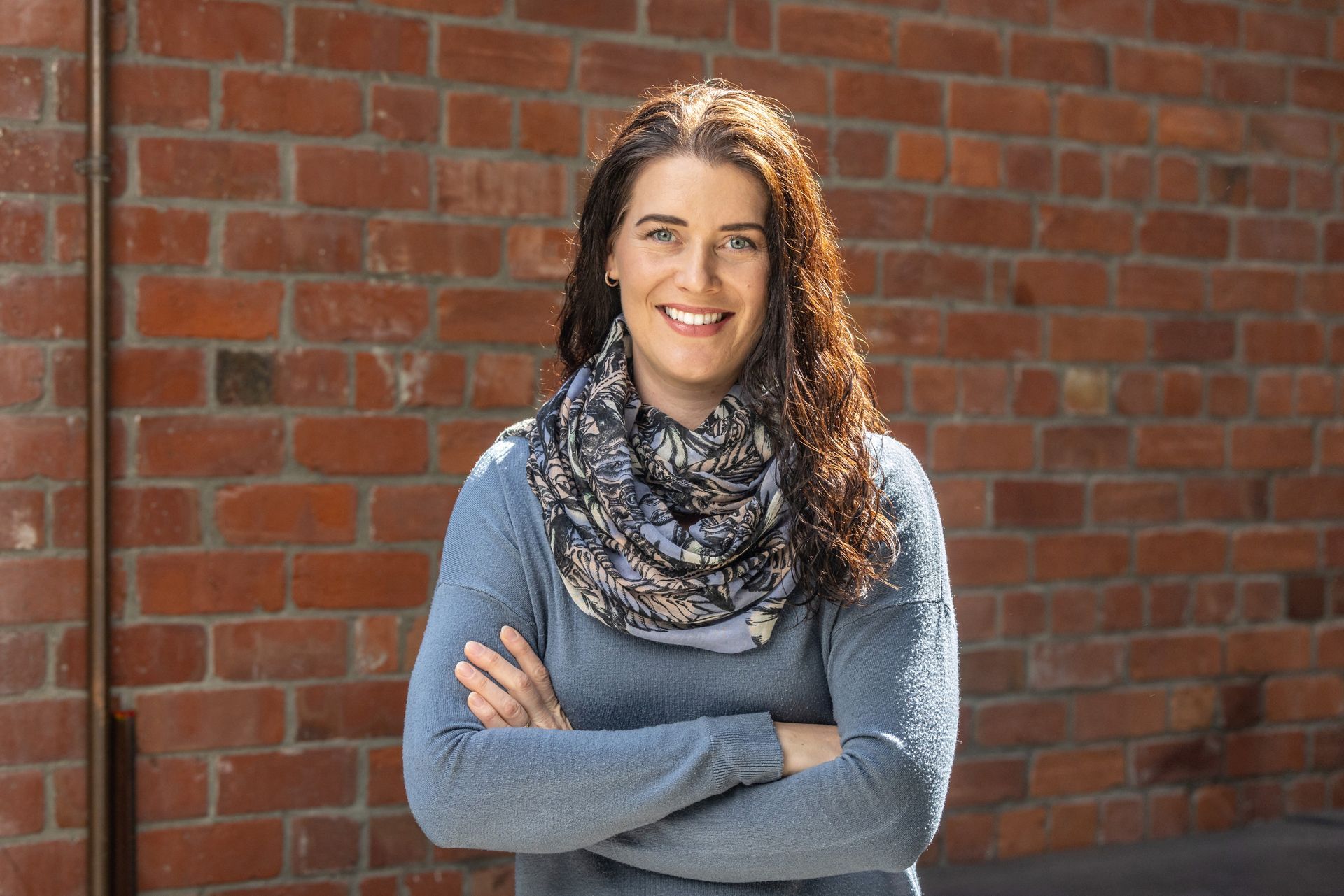 A woman is standing in front of a brick wall with her arms crossed.