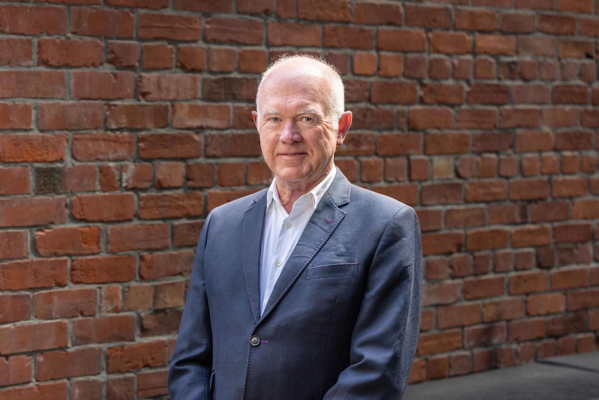 A man in a suit is standing in front of a brick wall.
