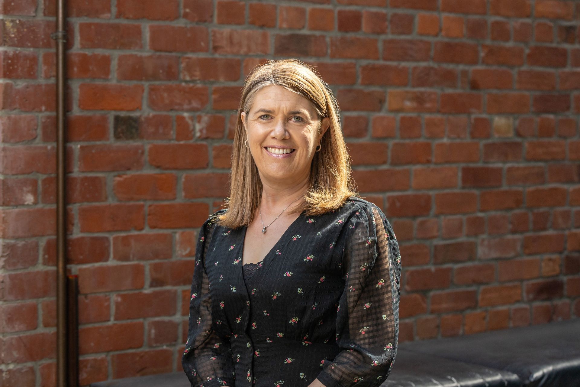 A woman in a black dress is standing in front of a brick wall.