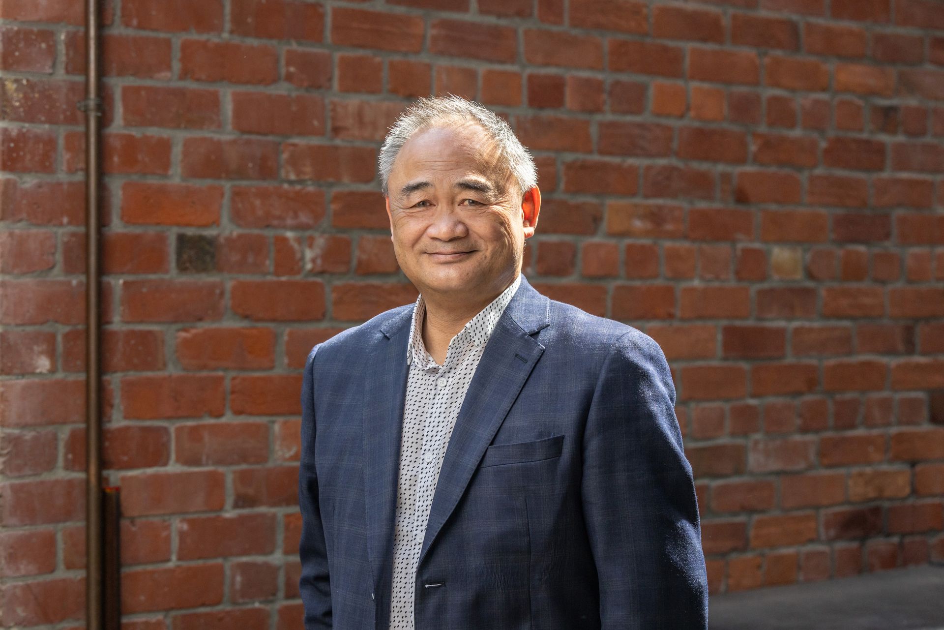 A man in a suit is standing in front of a brick wall.