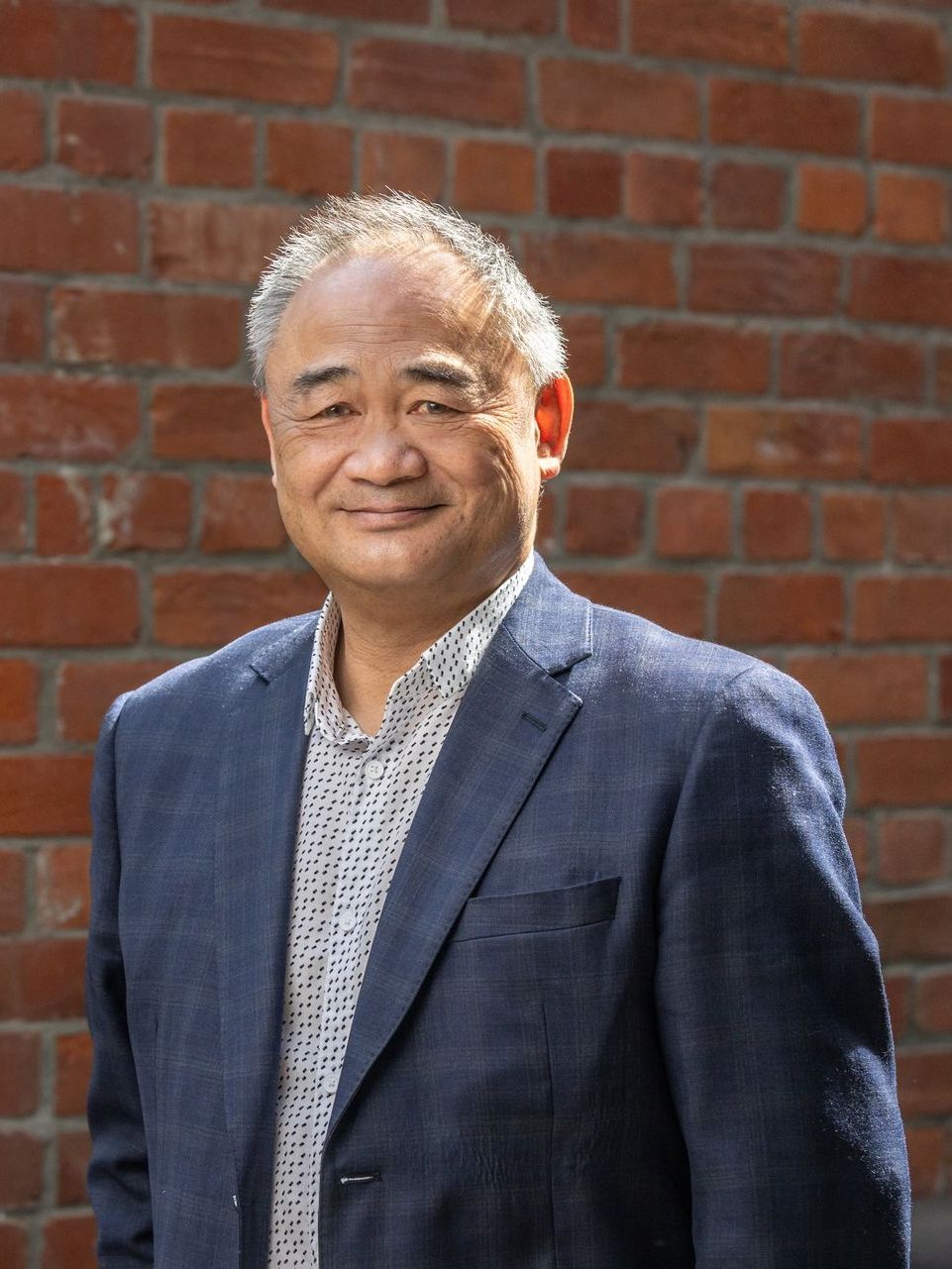 A man in a suit is standing in front of a brick wall.