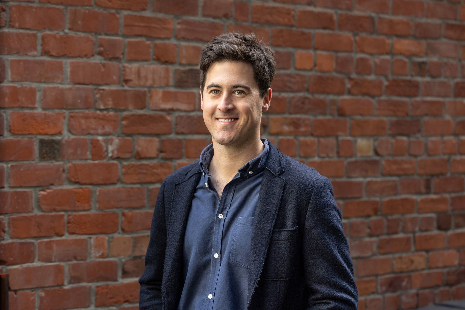 A man in a suit is standing in front of a brick wall.