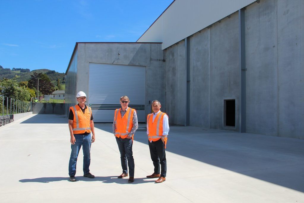 Three men in orange vests are standing in front of a large building.