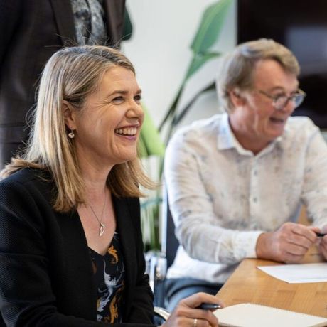 A woman is smiling while sitting at a table next to a man.