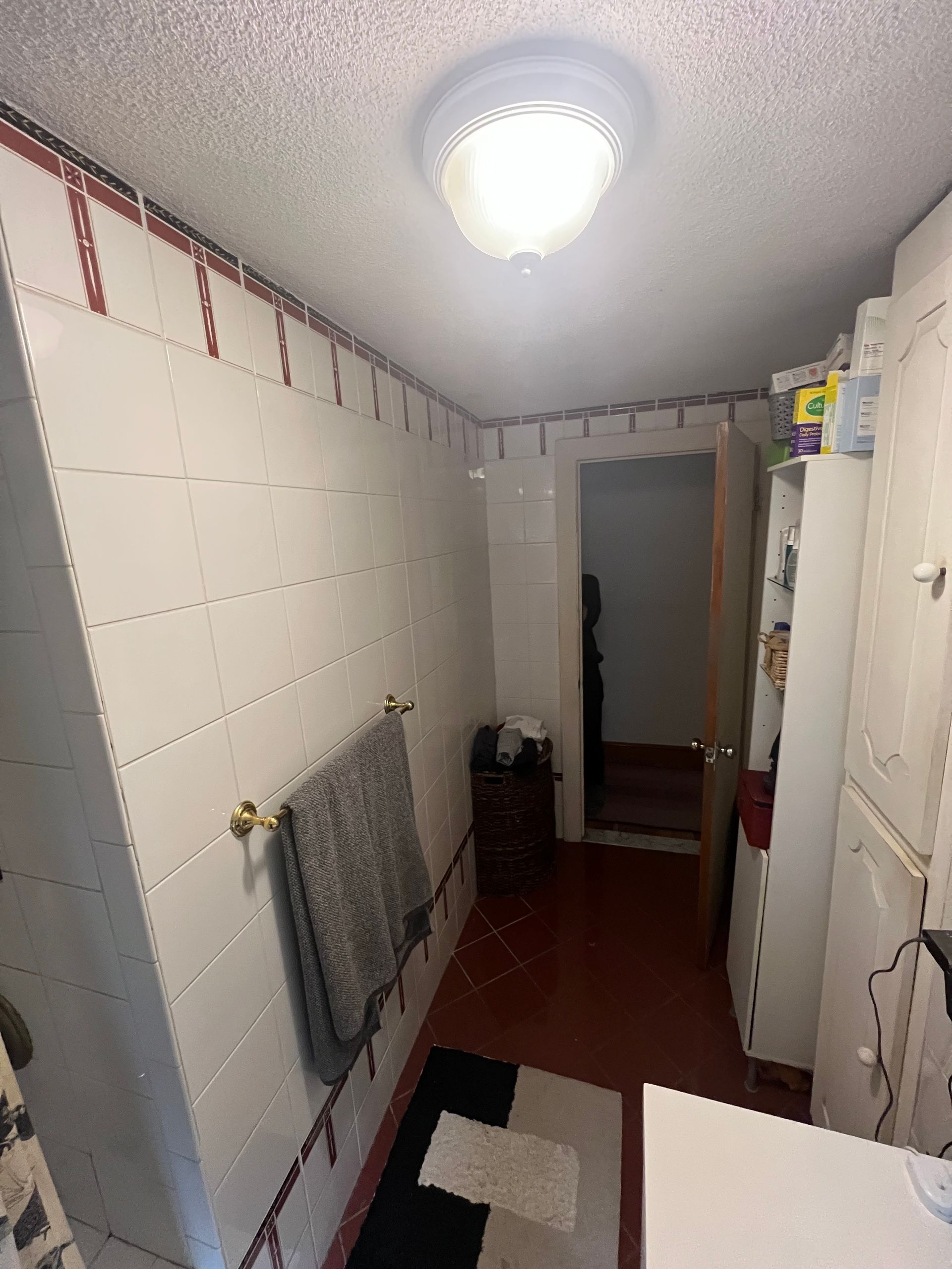 Outdated bathroom before remodel featuring white wall tiles with a red border, a basic white vanity, and red floor tiles. in Medford, MA