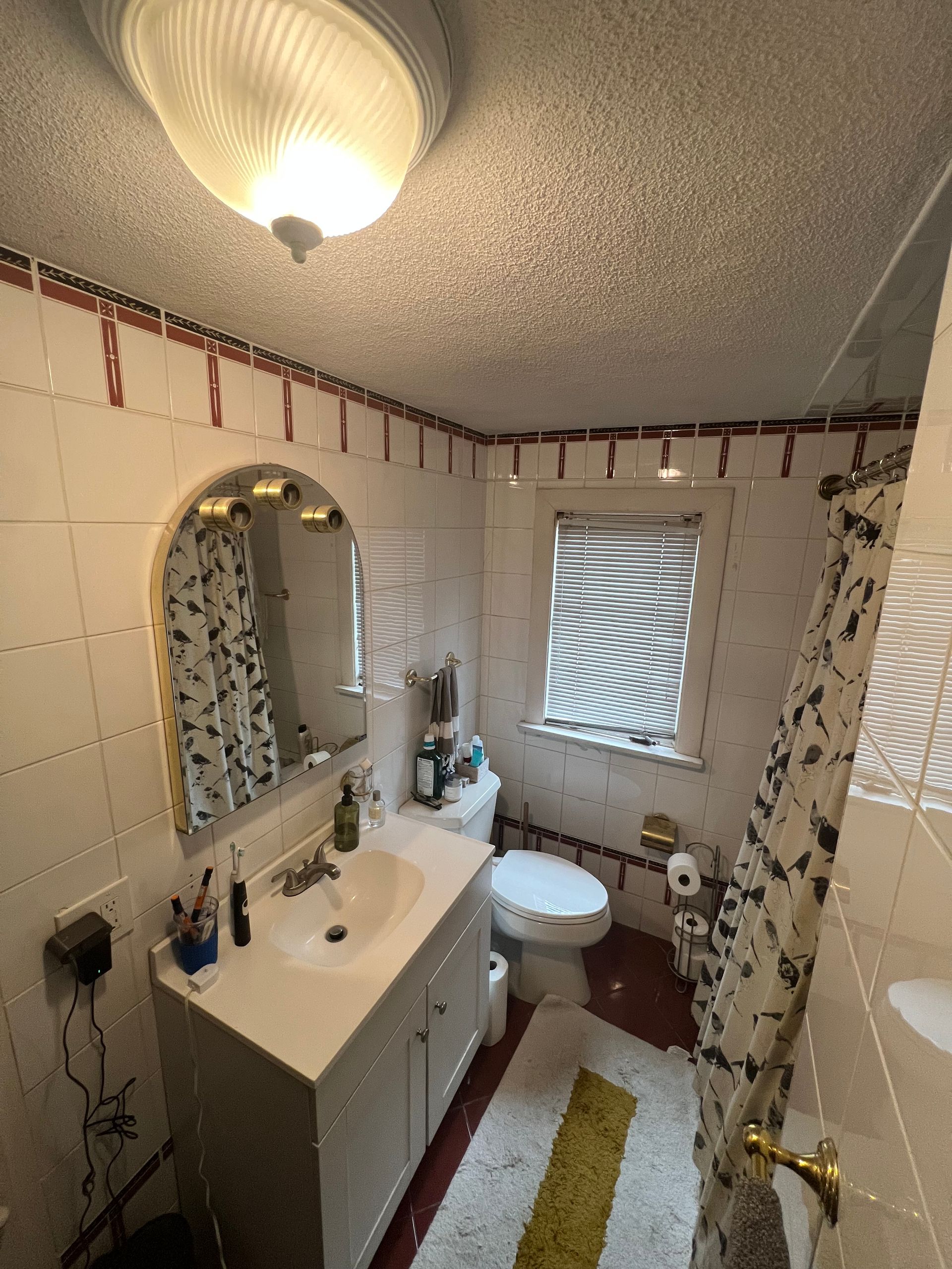 Medford, MA, Outdated bathroom before remodel featuring white wall tiles with a red border, a basic white vanity, and red floor tiles.