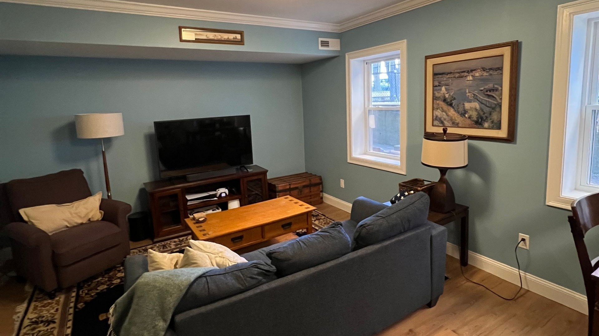 Finished basement living room in Boston with LVP flooring, blue gray walls, and new furniture after remodel