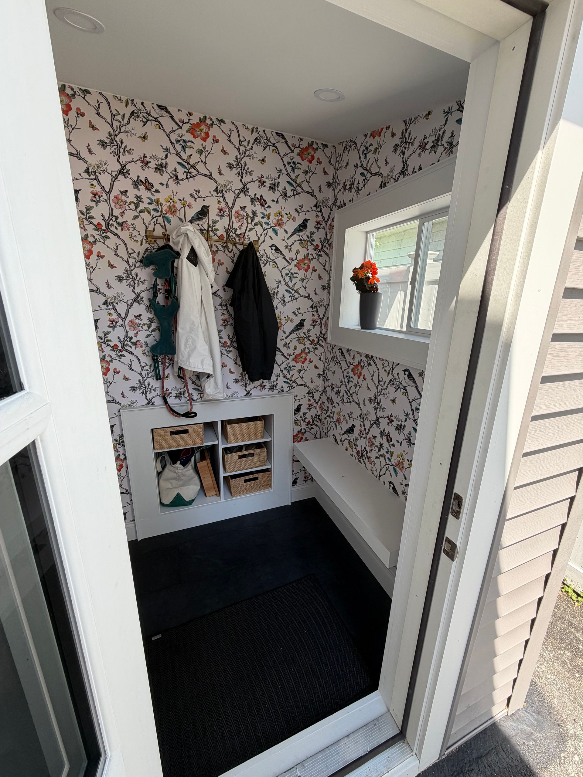 Finished mudroom with floral bird wallpaper, built-in storage cubbies with woven baskets,coat hooks.