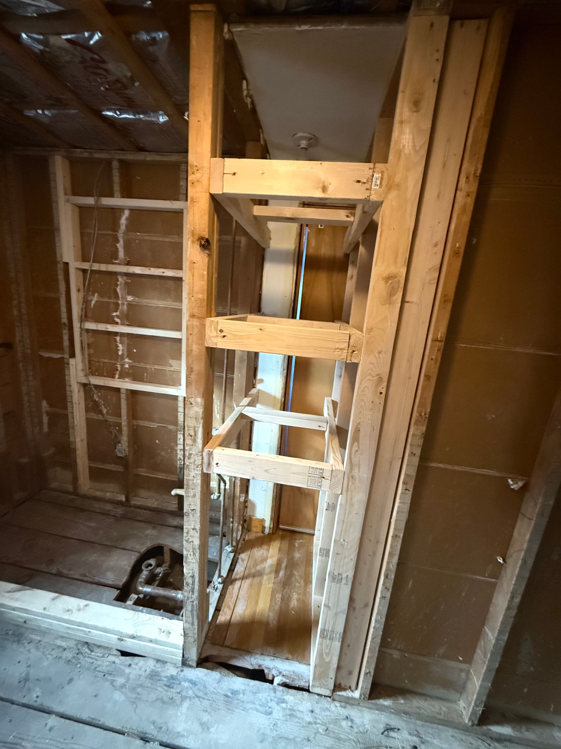 Bathroom stripped to the studs with a tool bag on the floor and the shower area prepped for plumbing.