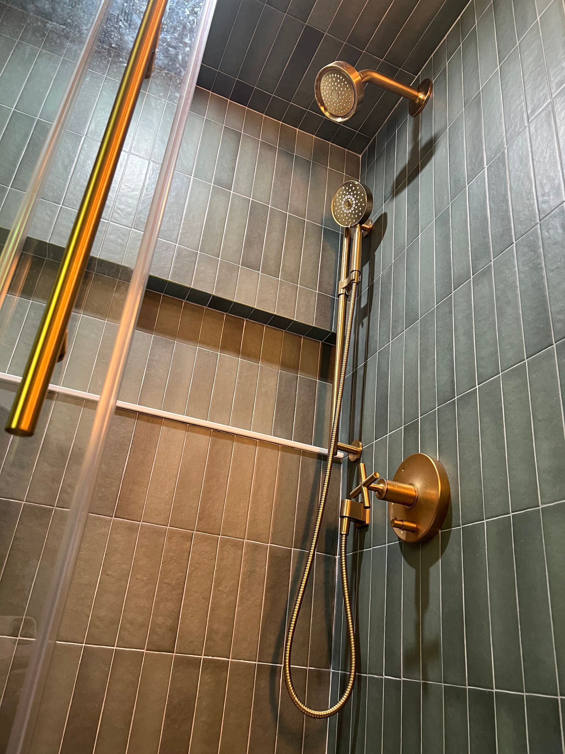 Detail shot of the shower corner during tile installation showing green vertical subway tiles and plumbing cutouts.