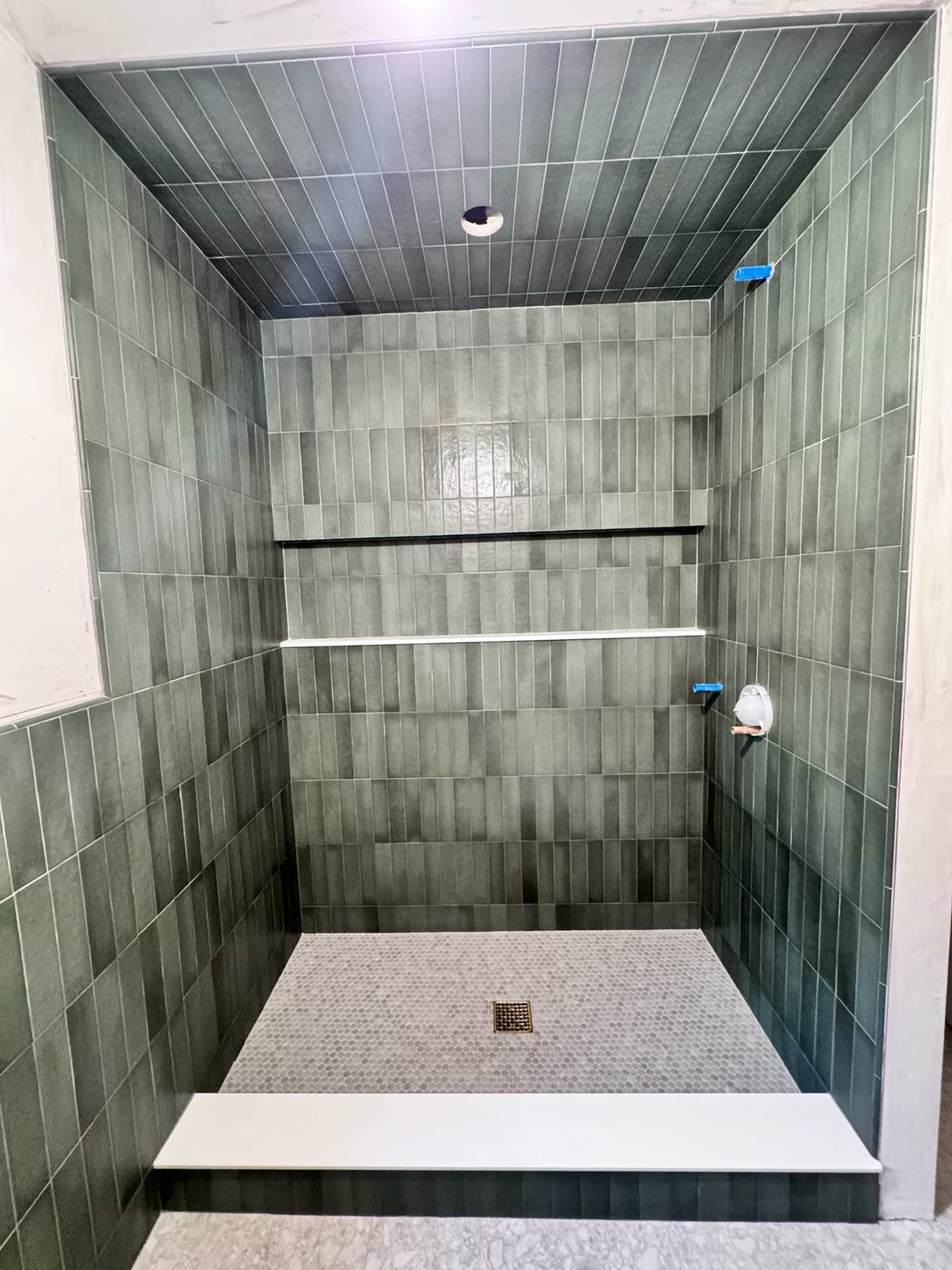 Completely tiled walk-in shower featuring green vertical tiles on the walls and ceiling, a recessed niche, and a hex tile floor