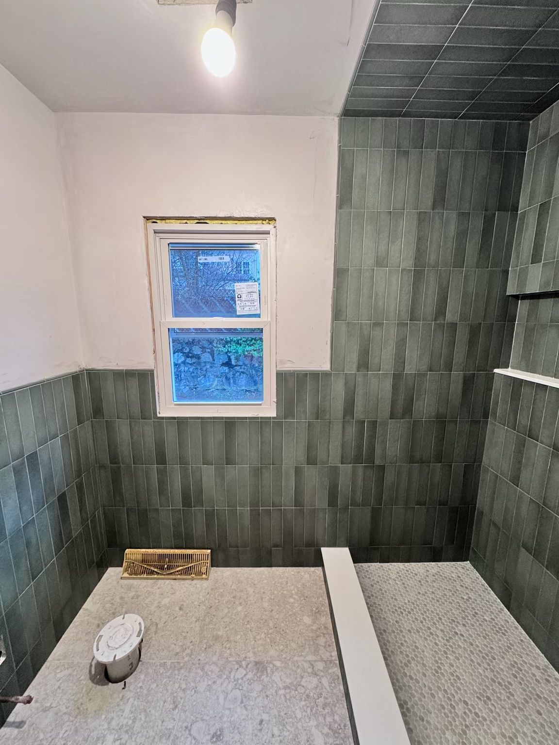 Bathroom remodeling progress showing green vertical wainscoting tiles installed around a window and a prepped shower pan.