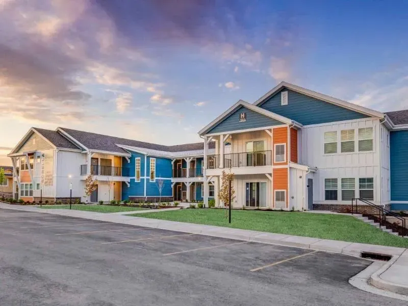 Exterior view of a colorful apartment community building with parking and green lawn.