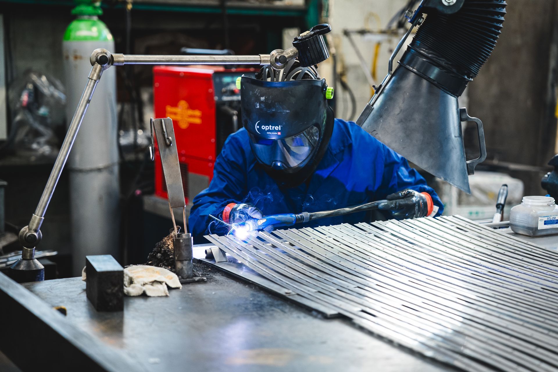 Saldatore in tuta blu e casco al lavoro con barre di metallo in un'officina. Scoppiano scintille.