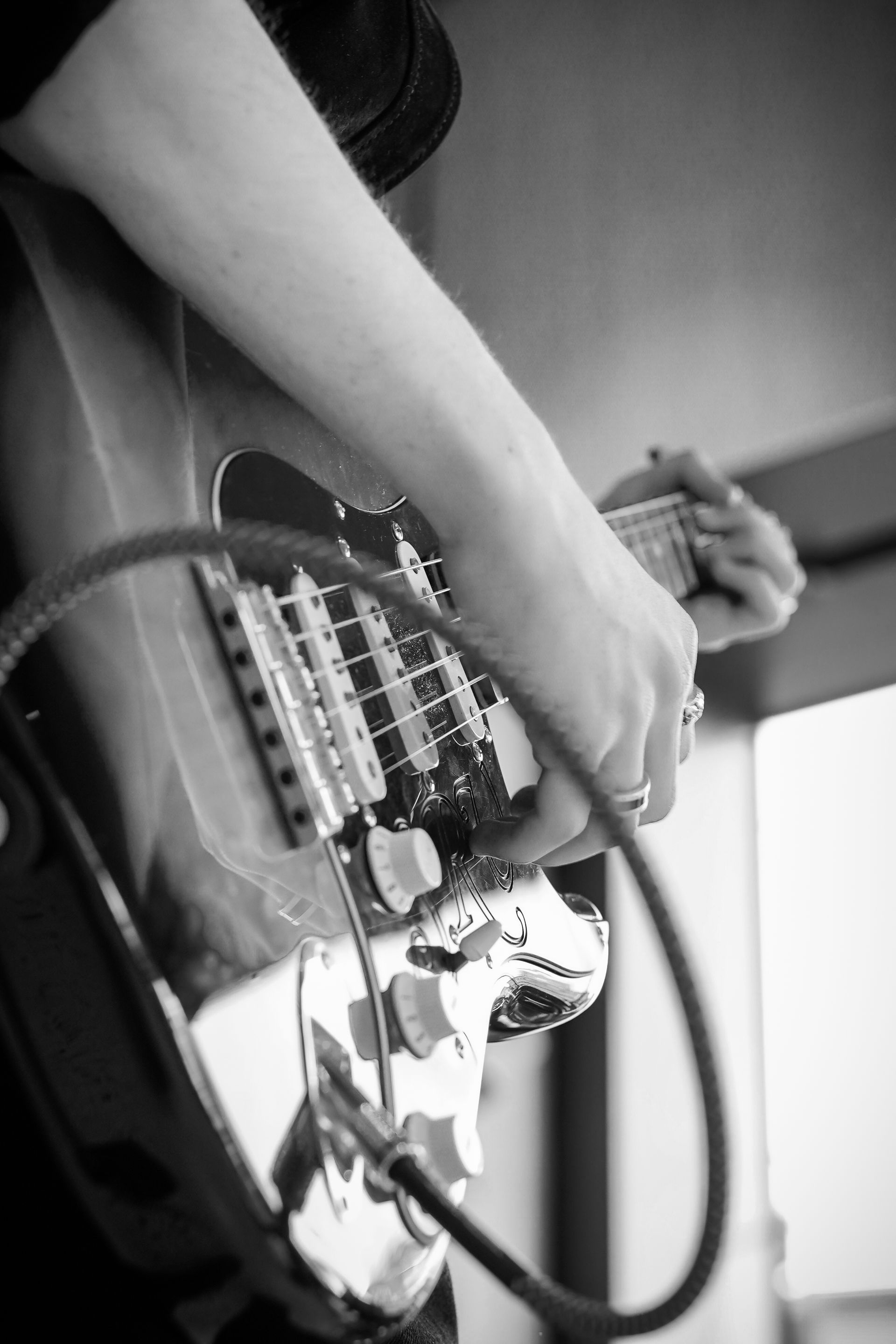 Person playing a sunburst electric guitar with white pickups and a green instrument cable plugged in