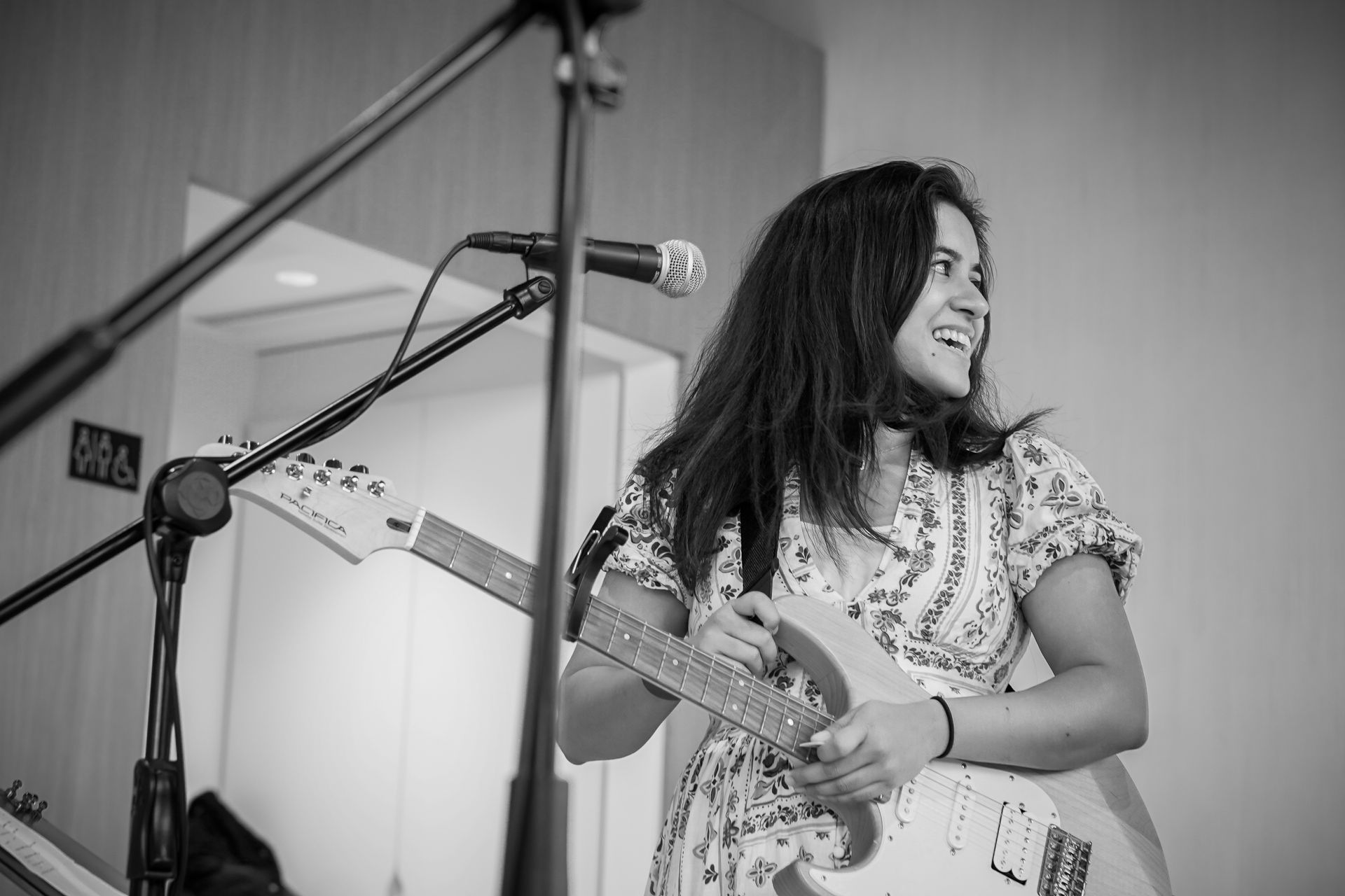Musician smiling while playing guitar and singing into a microphone on stage