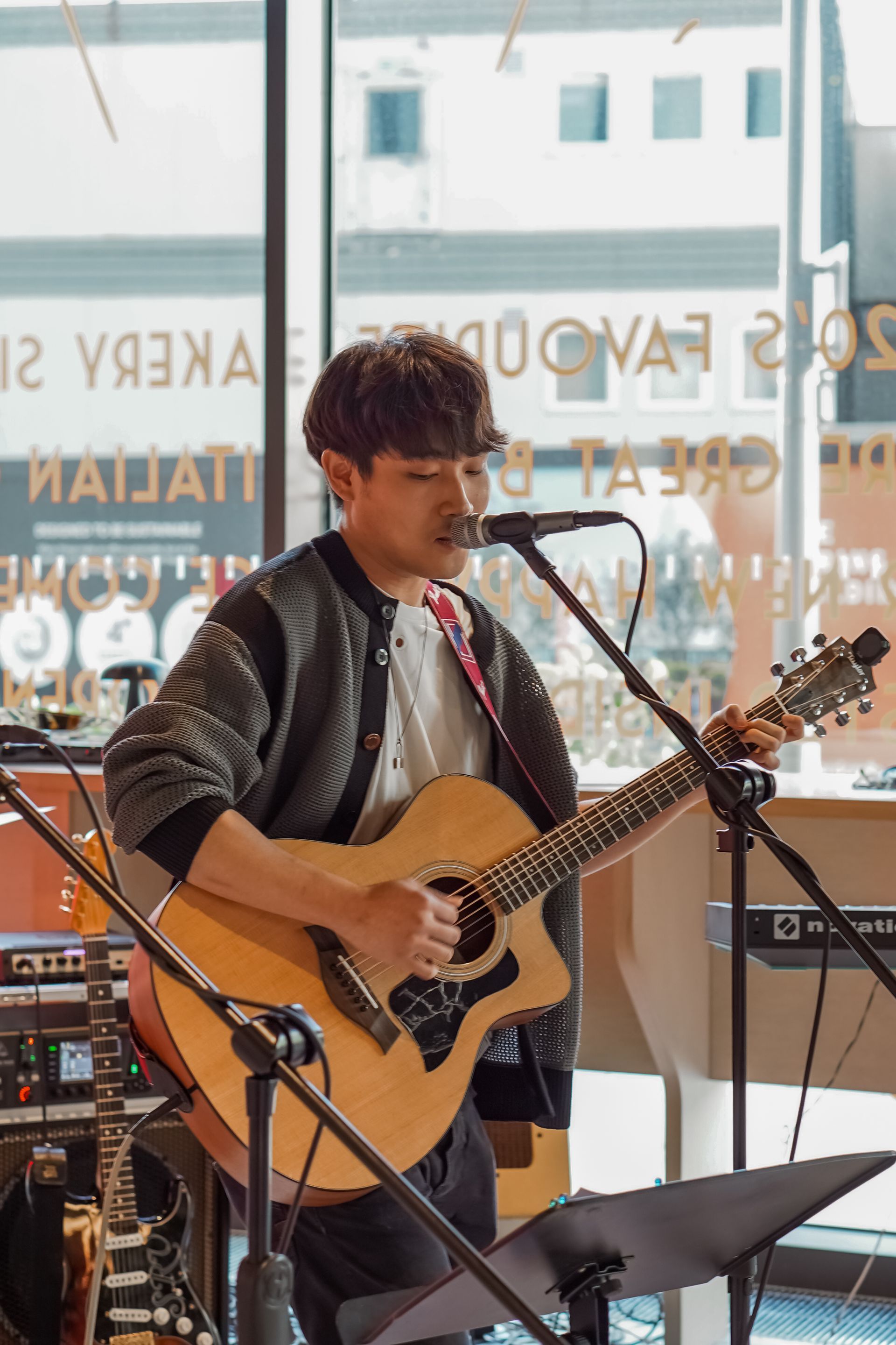 Musician singing and playing acoustic guitar in a café by a microphone stand
