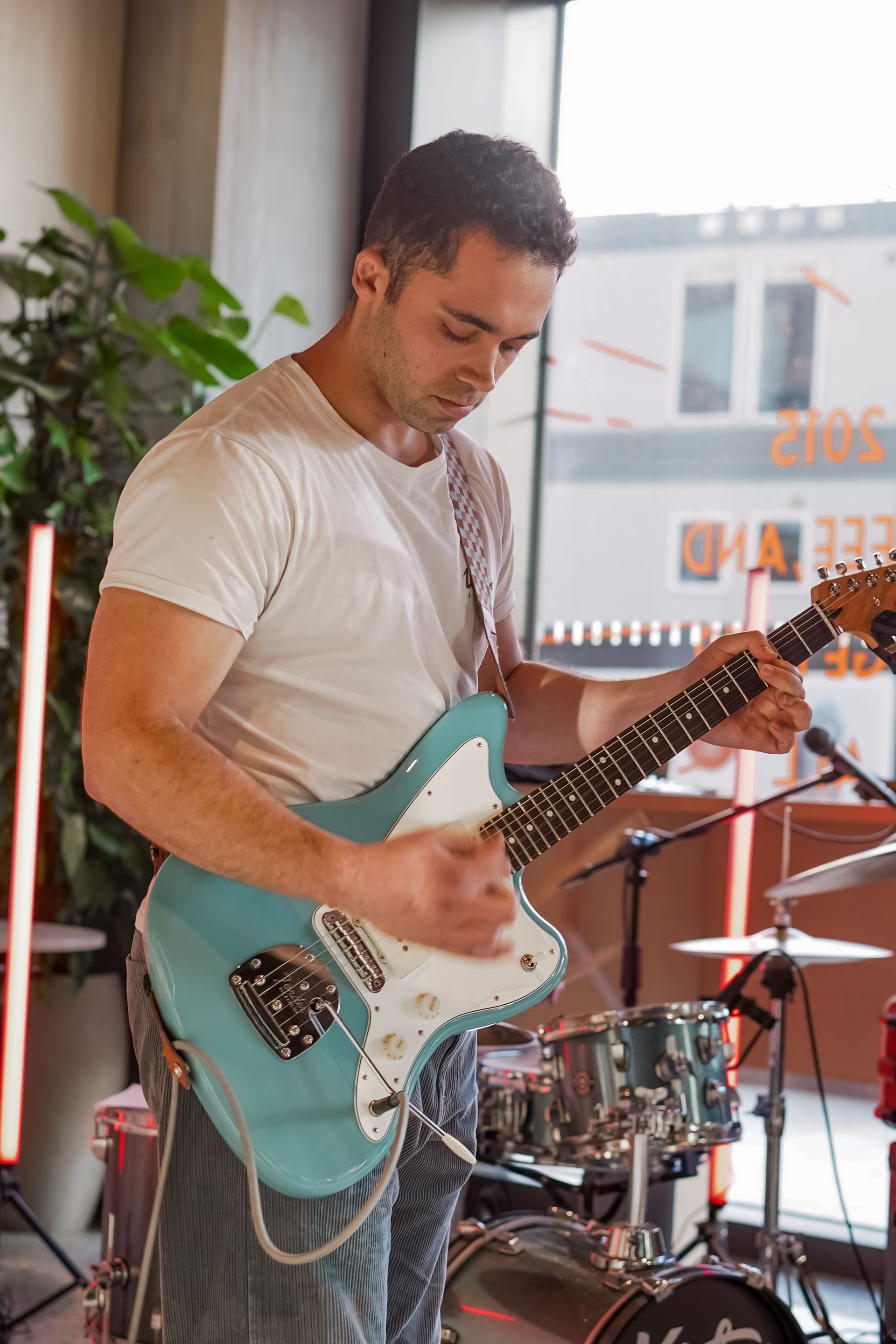 Man playing a turquoise electric guitar near a window in a music studio