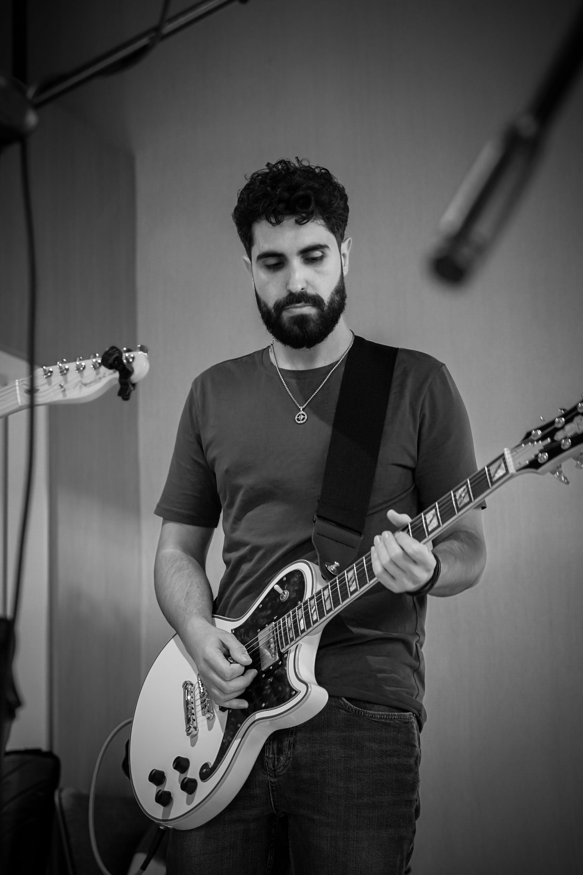 Man playing electric guitar on stage in a dark shirt, standing before a microphone