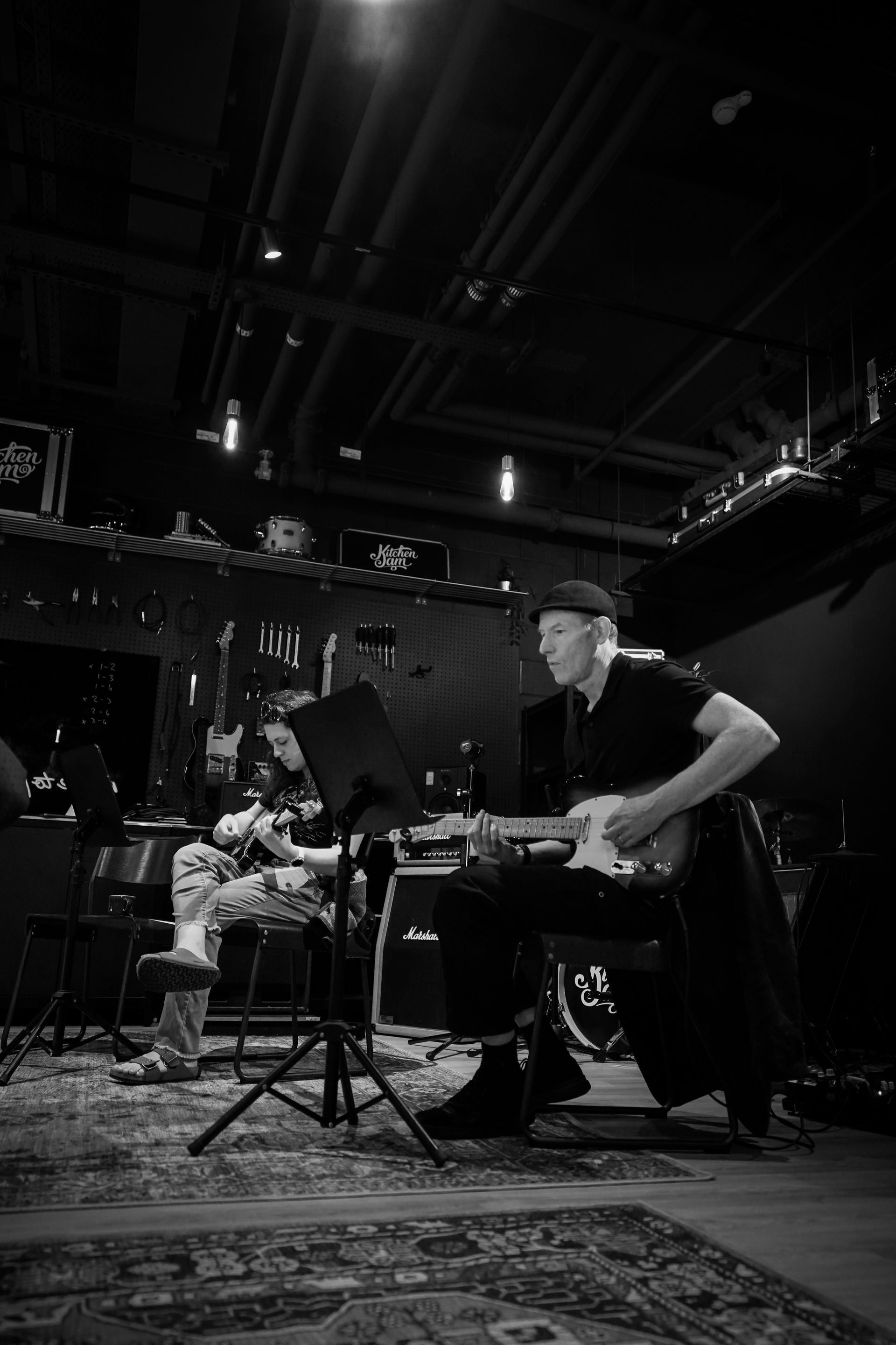 Musicians rehearsing on a dimly lit stage with drums, guitar, and music stands