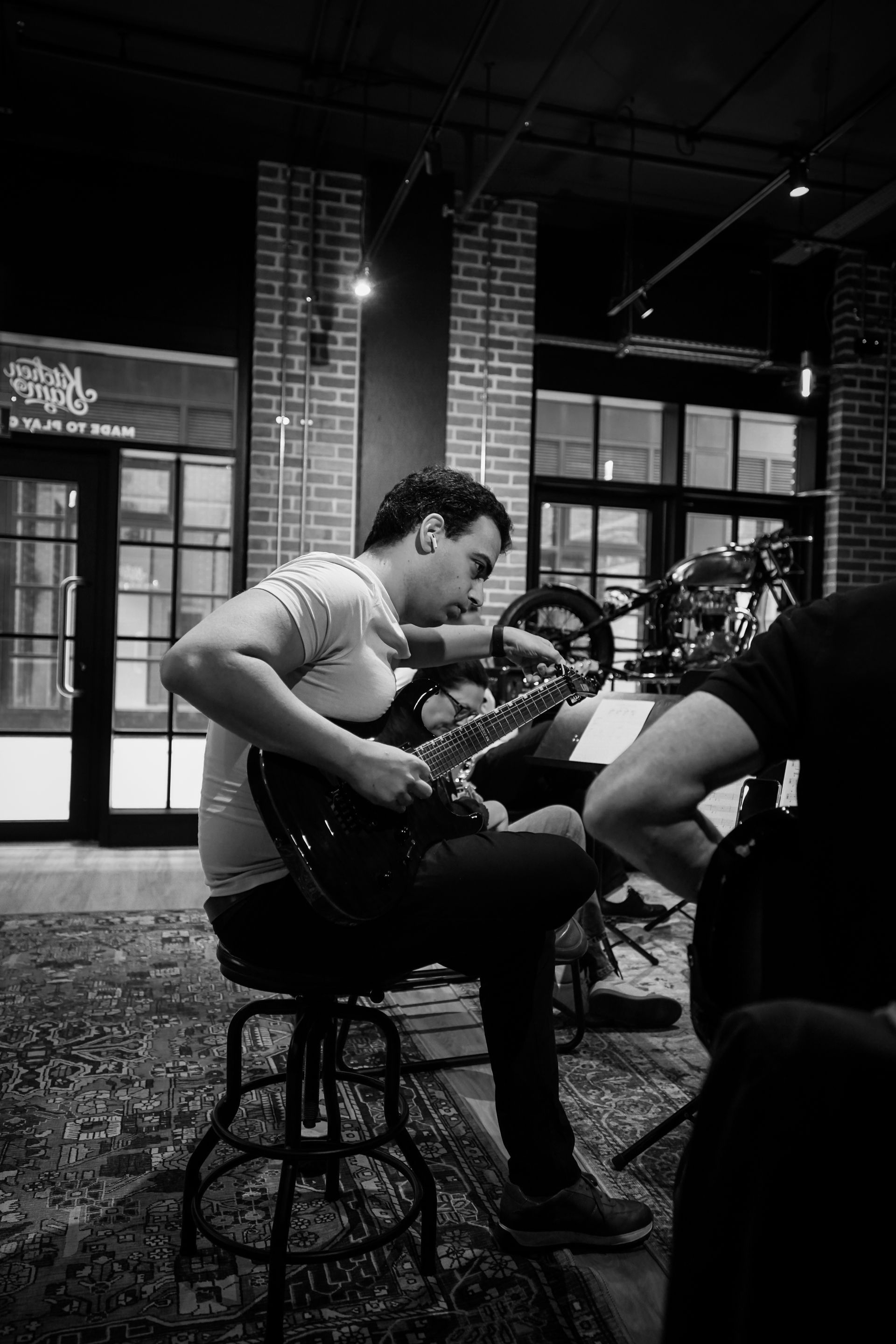 Man playing guitar on a stool in a dimly lit indoor venue