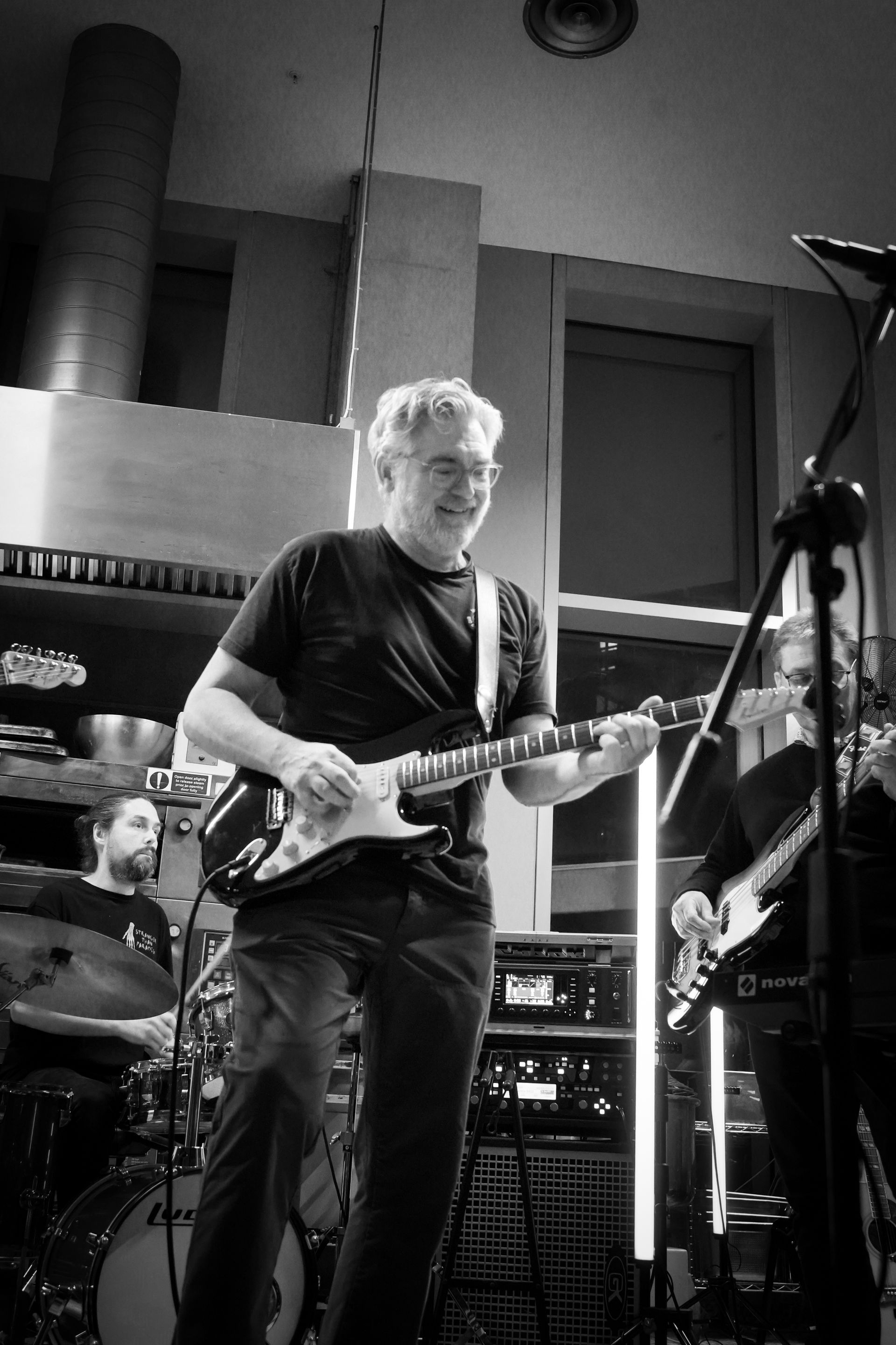 Man playing electric guitar onstage with band. Black and white photo.