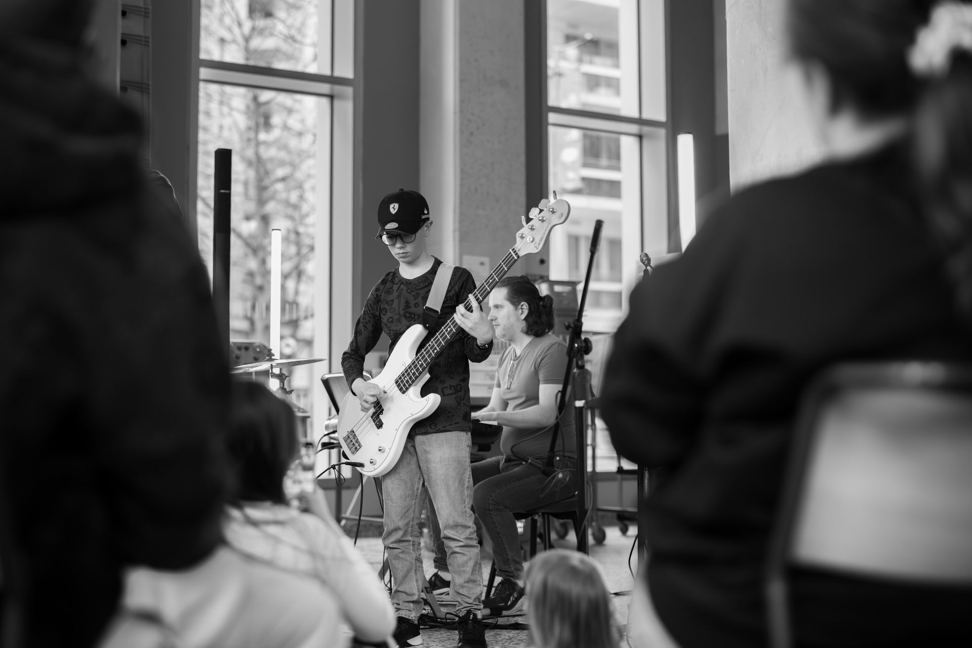 A black and white photo of a boy playing a guitar in front of a crowd.