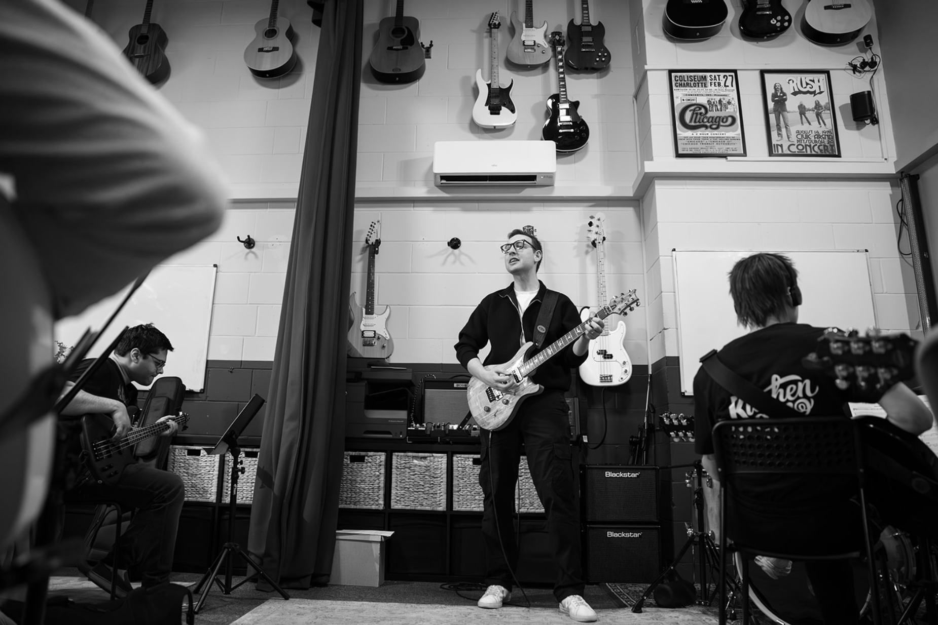 A guitar teacher is playing a guitar in front of a group of people.