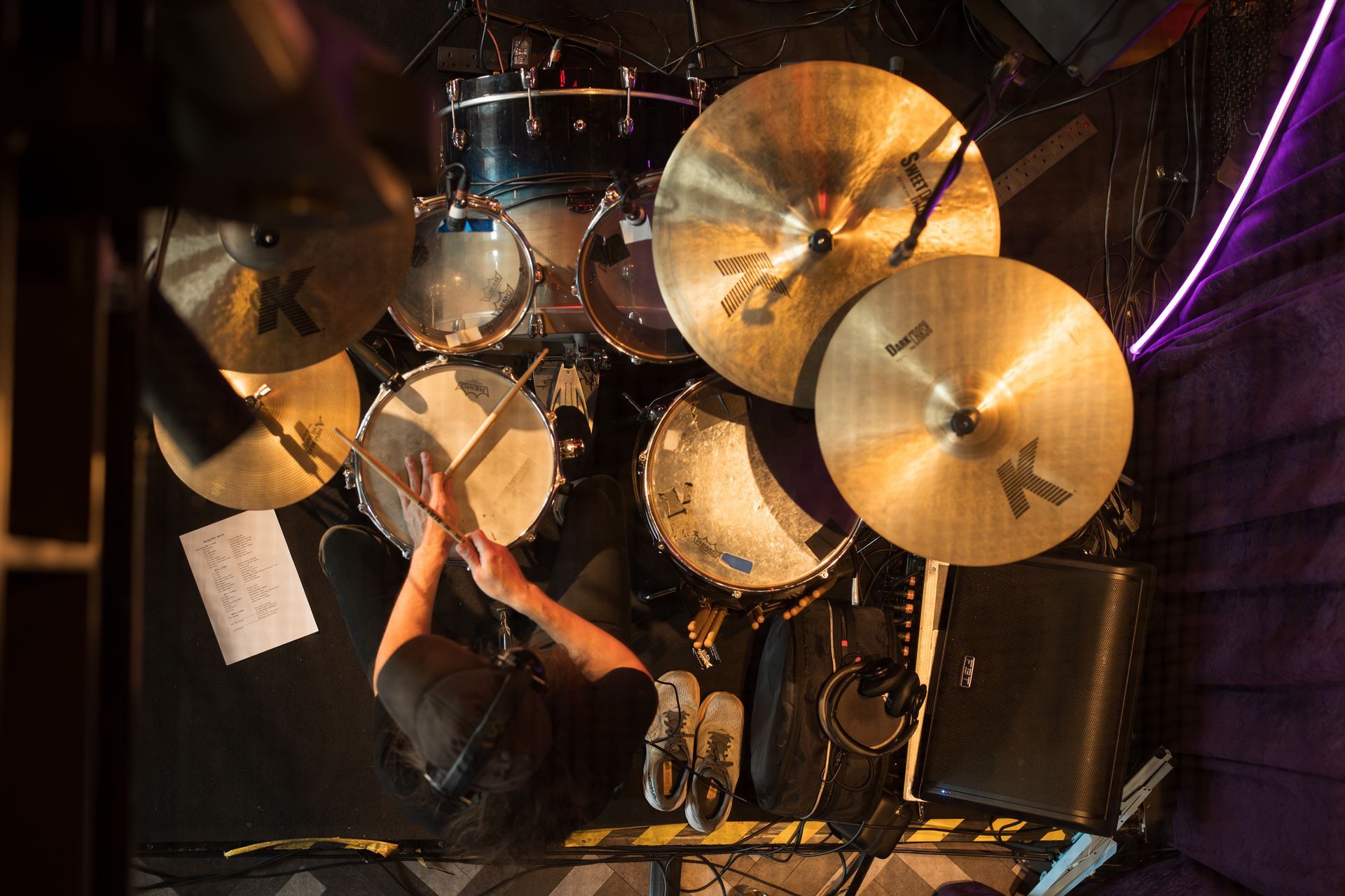 Musician playing an orange bass guitar beside a drum set indoors