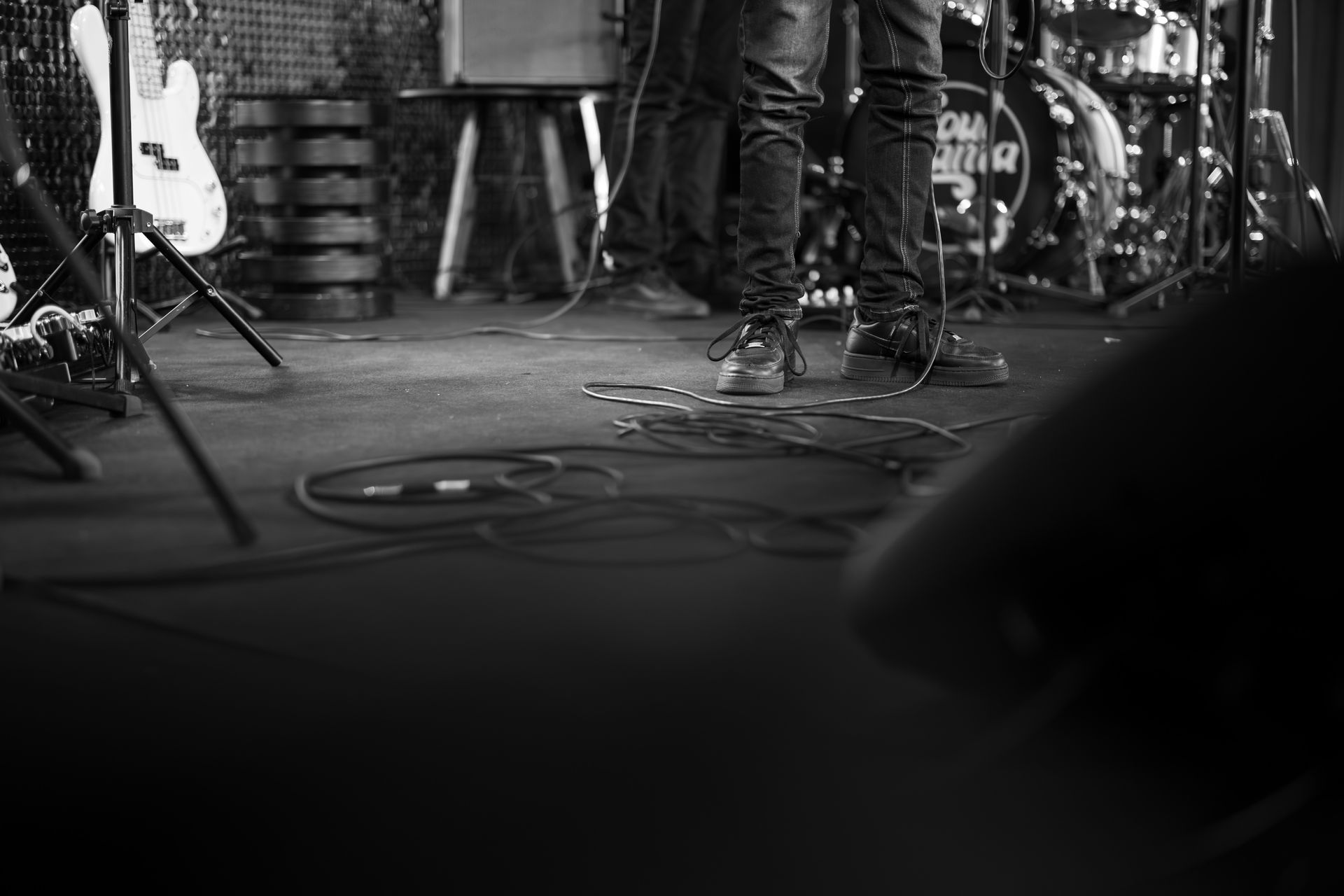 Black-and-white view of a live music stage with drums, microphone stands, guitar, and coiled cables