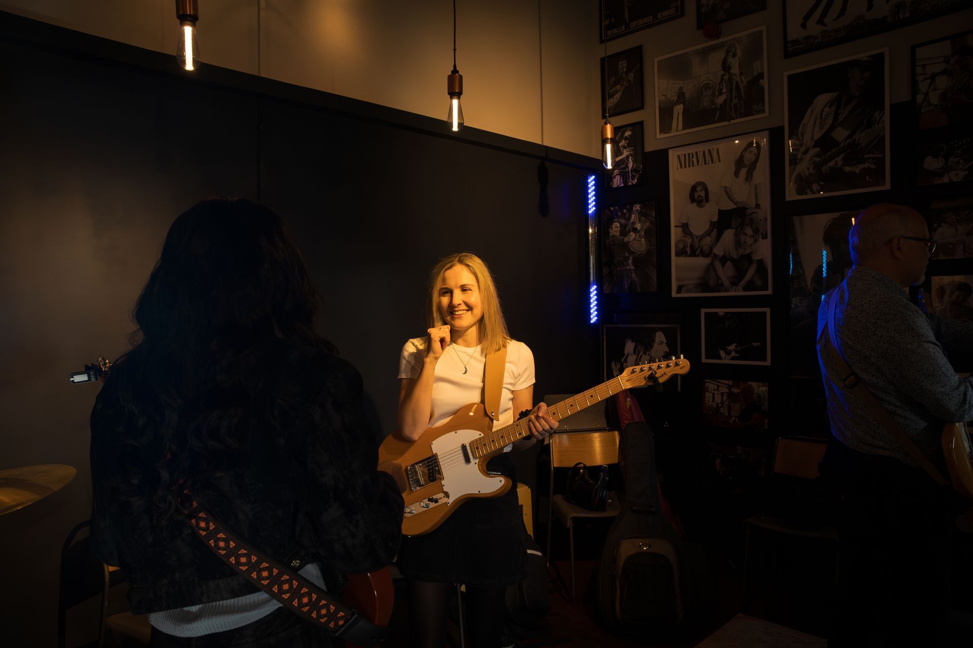 Singer performing onstage with a white guitar in a dimly lit bar, band members in the background