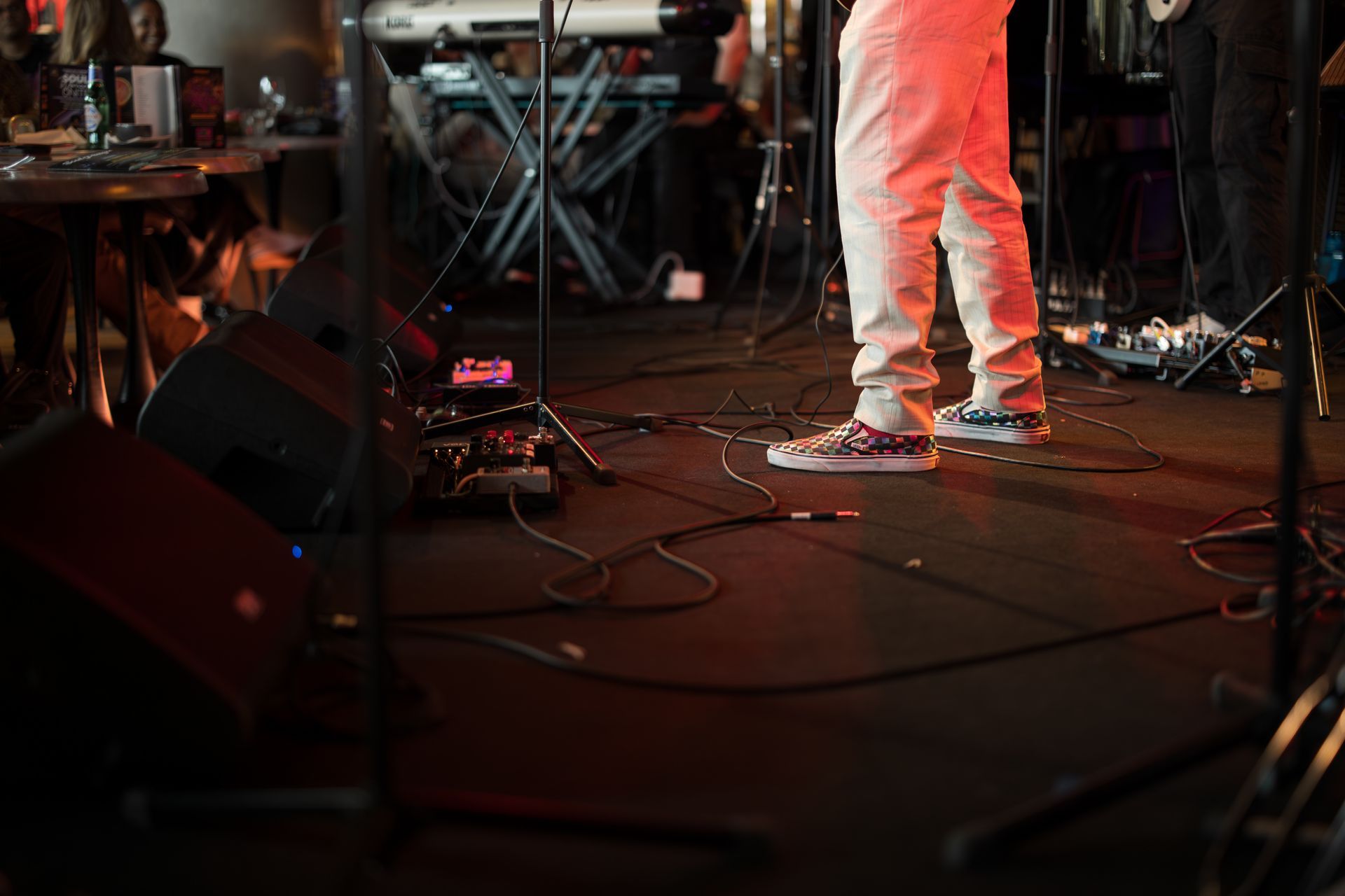 Low-angle shot of a musician on stage with cables and guitar pedals.