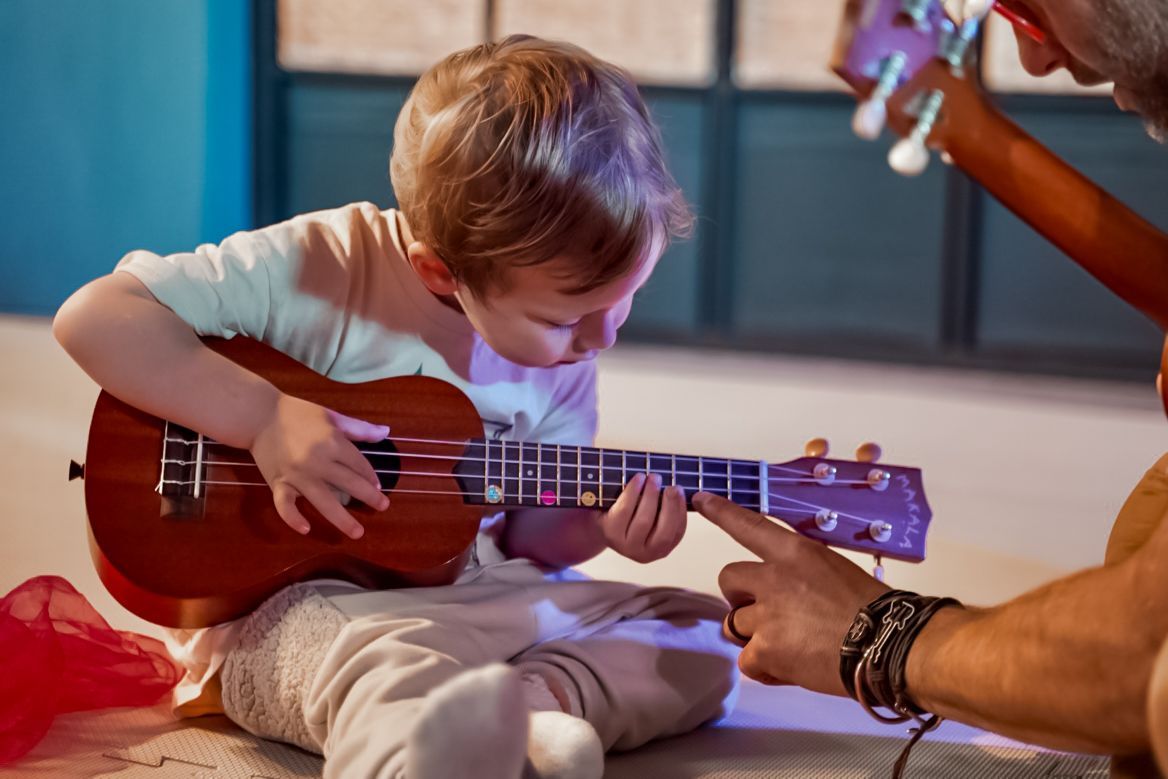 A focused toddler learning how to play the ukulele