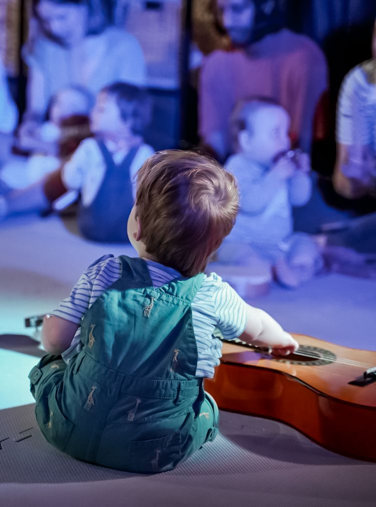 Baby watching the baby concert, holding a guitar
