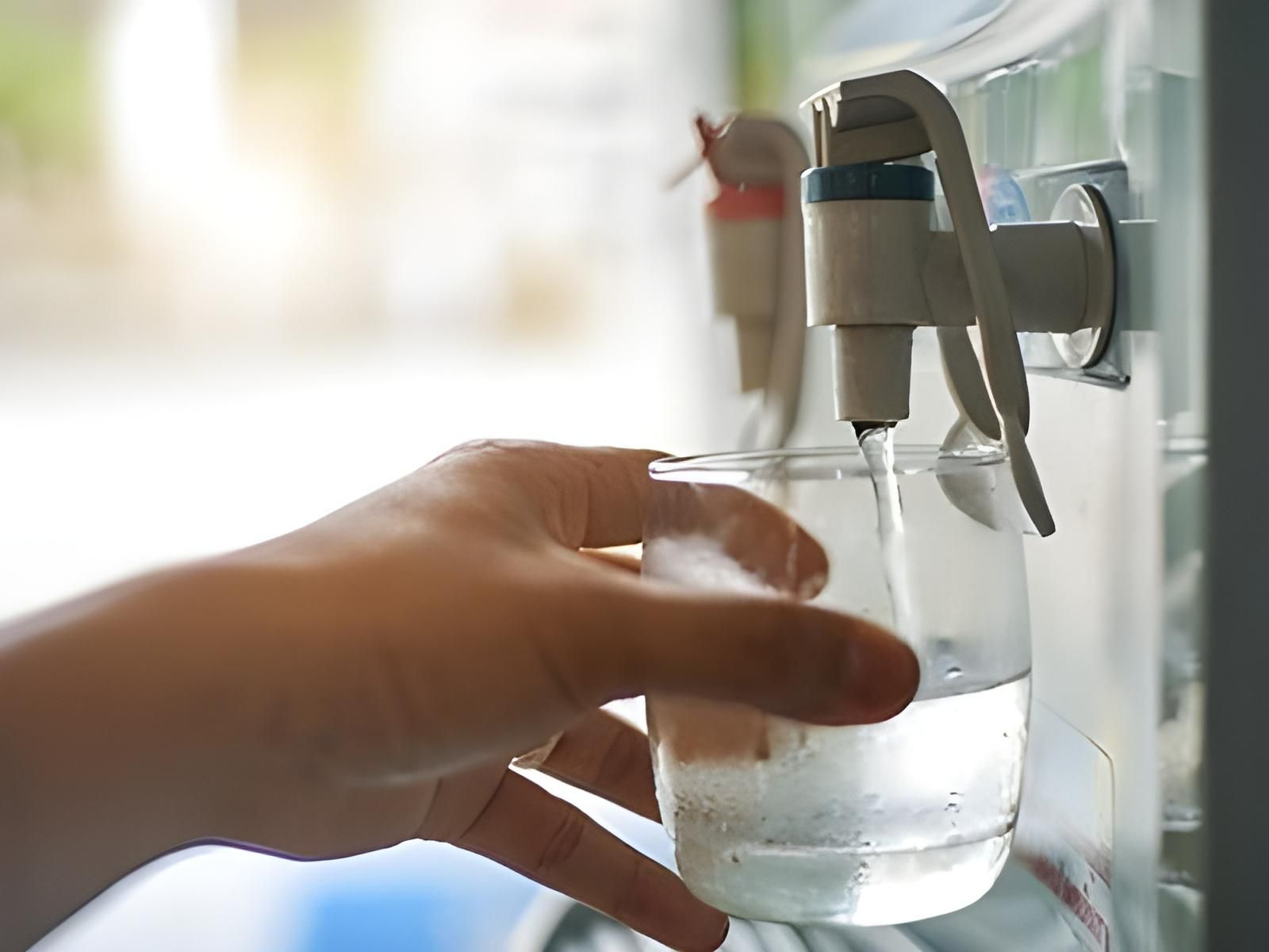 A Person is Pouring Water Into a Glass From a Water Dispenser — NT Water Filters In Winnellie, NT