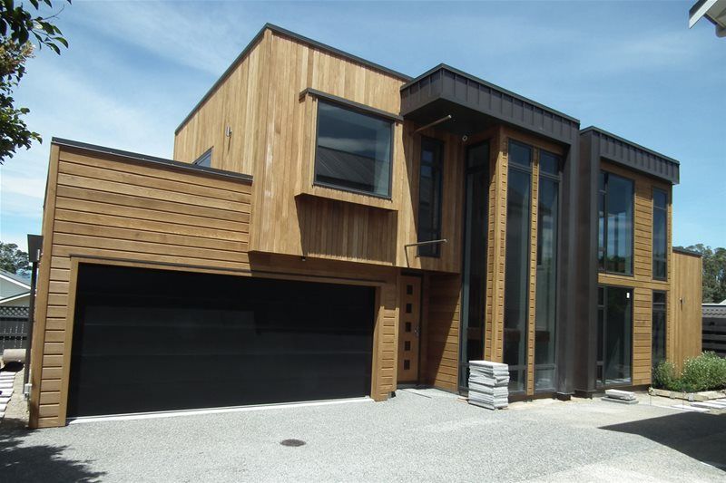 Modern wood-clad house with a large black garage door and tall glass entryway