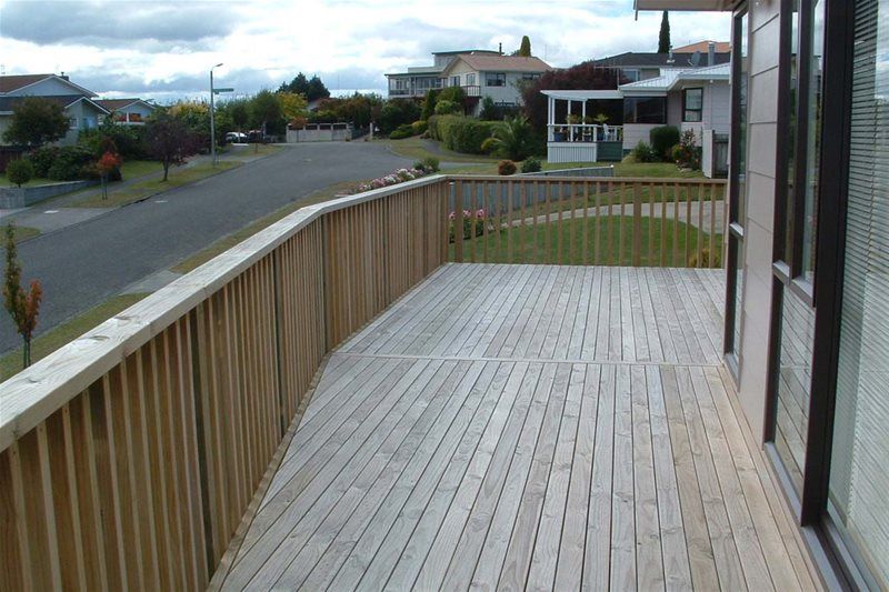 Empty wooden deck with railing beside a residential street and houses on an overcast day