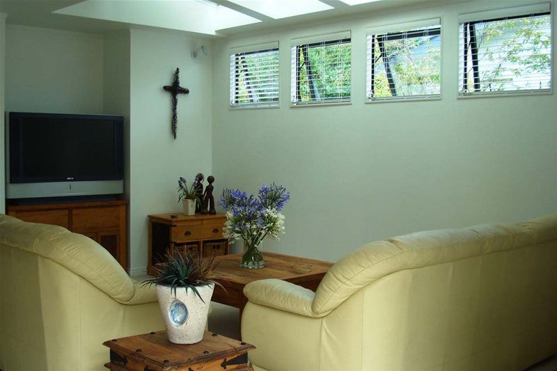 Living room with cream sofas, TV, wall cross, wooden furniture, flowers, and narrow windows