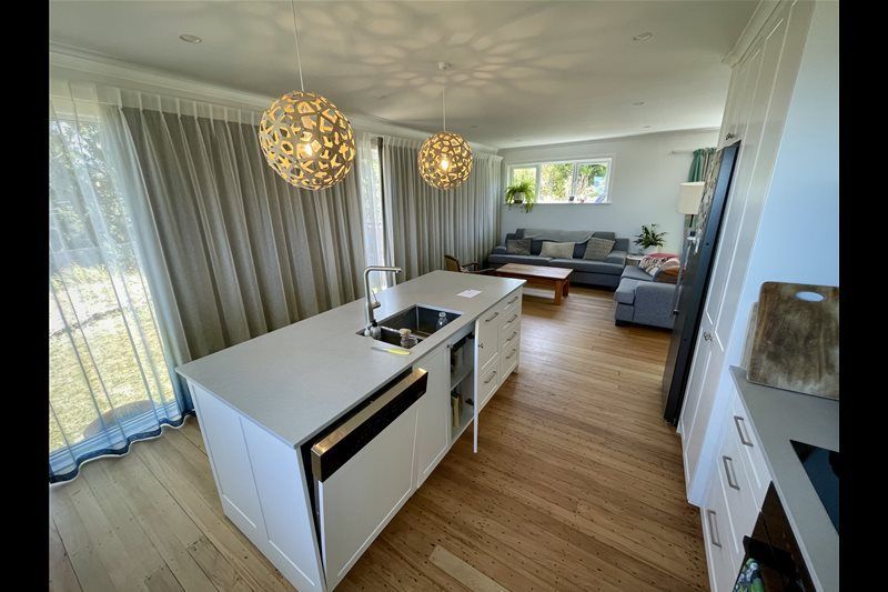Modern open-plan dining and living room with white island, pendant lights, gray sofa, and large windows