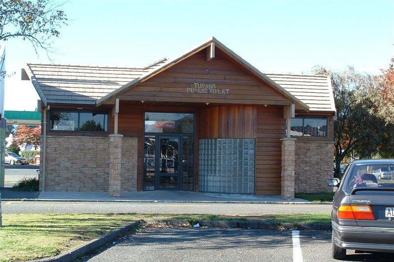Small brick building with a peaked roof and glass entrance, seen from a parking lot.