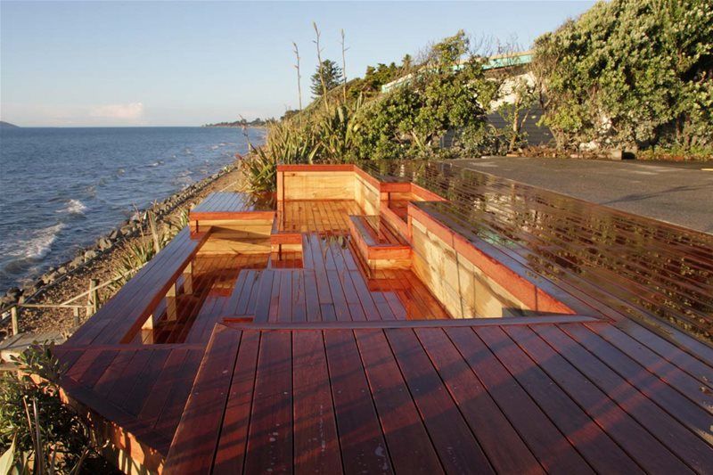 Wooden oceanfront deck beside a rocky shoreline, with a view over the water and trees.