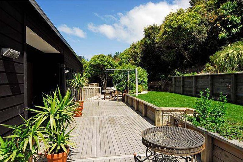 Wooden deck patio with potted plants, outdoor table, and green lawn beside a house