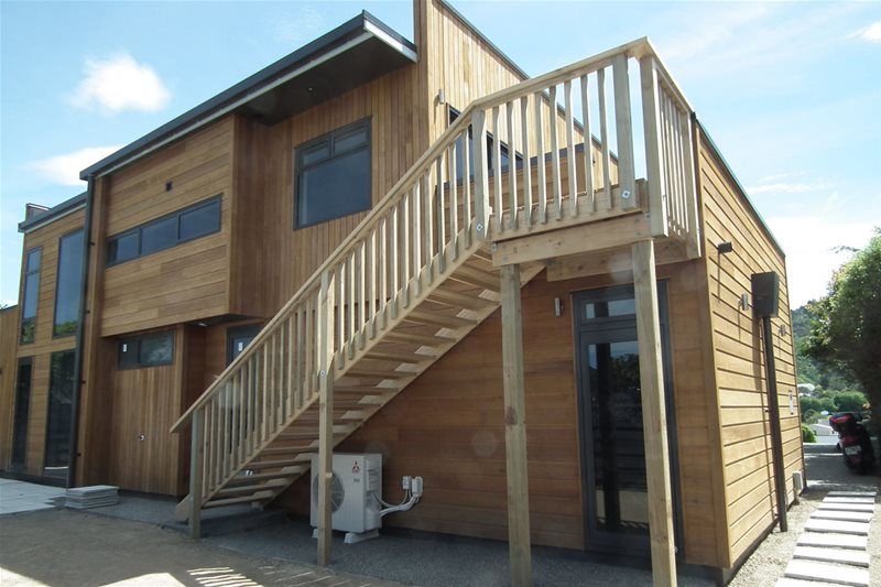 Wooden two-story house with exterior staircase and balcony, viewed from the front corner