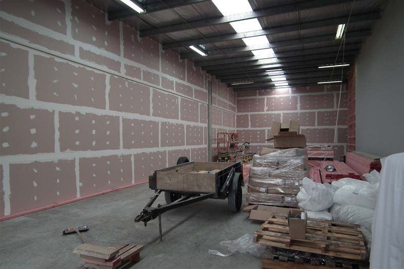 Unfinished warehouse interior with drywall walls, stacked materials, and a wheelbarrow on concrete floor.