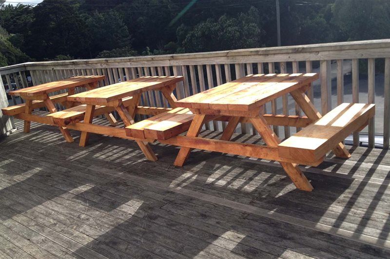 Three wooden picnic tables on a sunlit deck with a railing overlooking trees