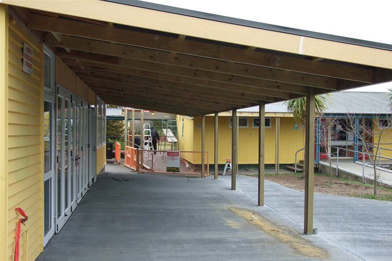 Covered walkway beside a yellow building, with metal posts and a paved path leading outdoors