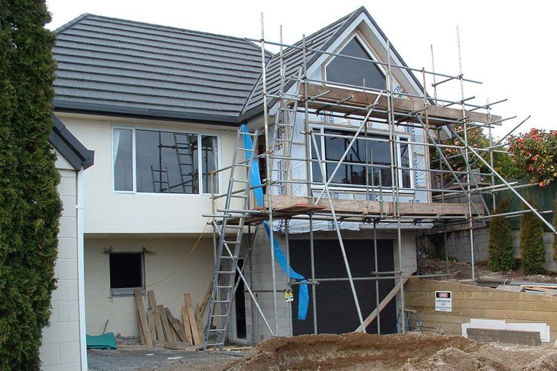 House exterior under construction with scaffolding and blue protective sheeting in front of the upper windows.