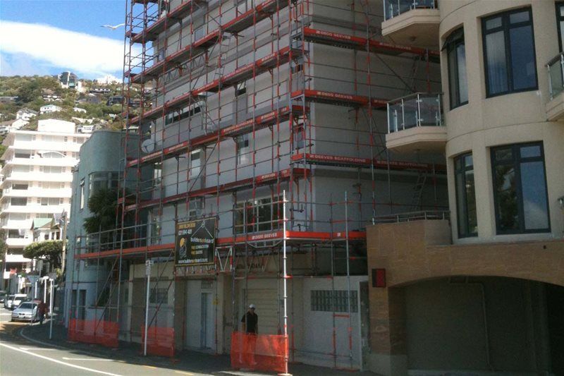 Scaffolded building under construction on a city street beside neighboring apartments