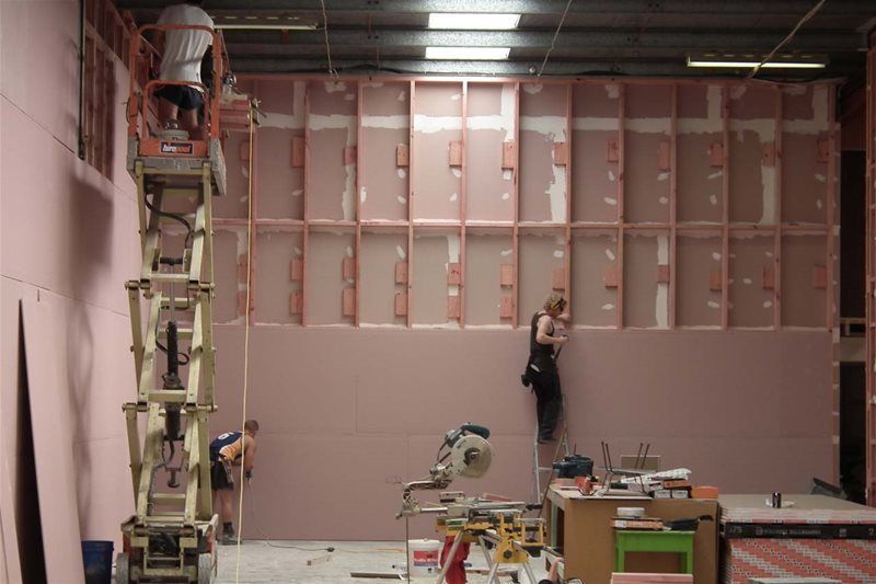Workers installing large wall panels in an unfinished room with scaffolding and tools.