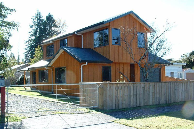 Wooden two-story house with blue trim and a fenced yard on a sunny street.